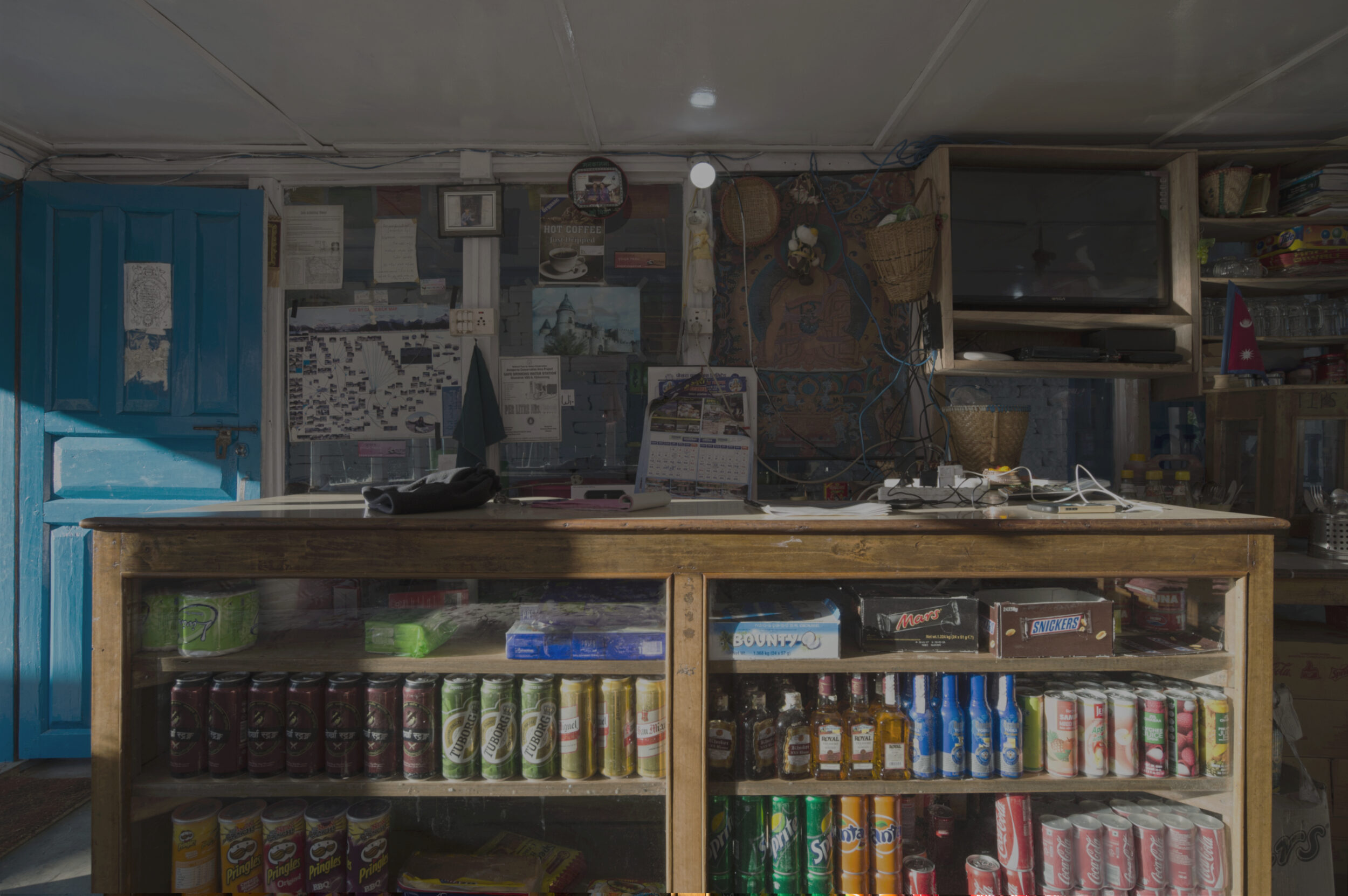 lodge front desk, shelves of drinks and candy, electrical wires, tv, wall covered with papers and posters