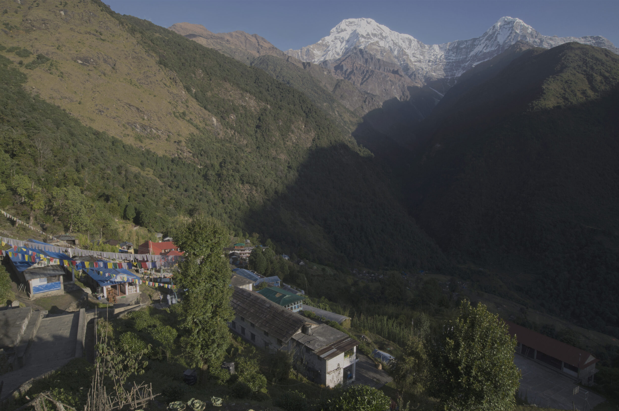 small town in a narrow valley, stone structures, green mountains, and snowy peaks