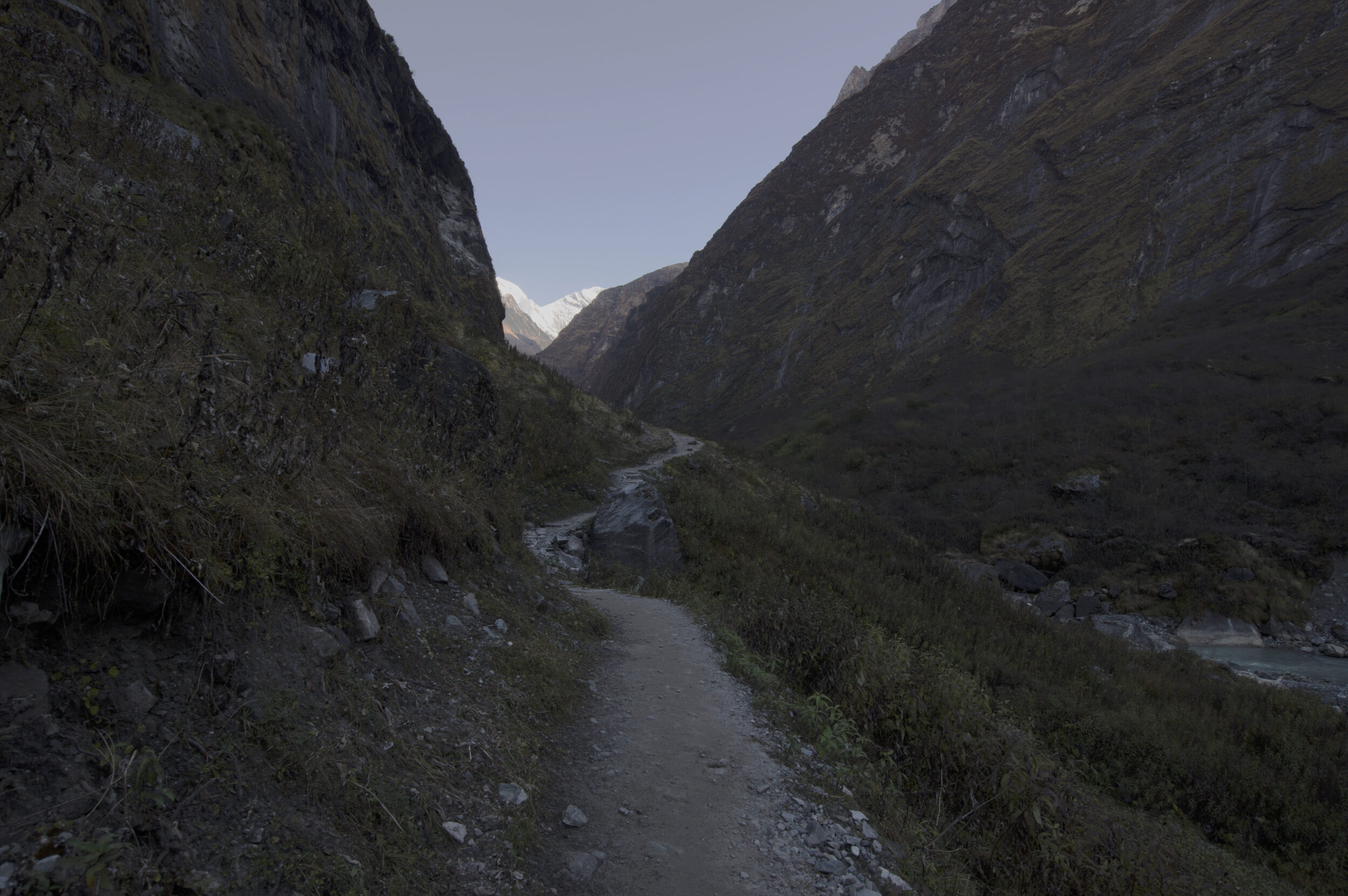 early morning, a trail in shadows, mountains on either side, snow-covered Himalayan peaks in the distance